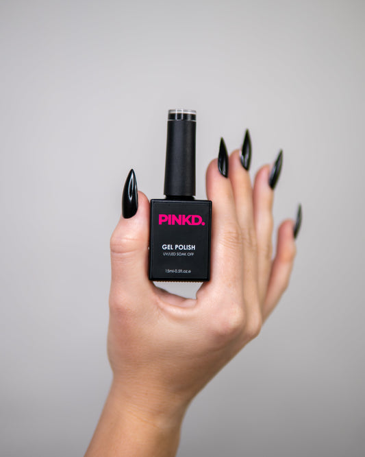 Hand holding a black nail polish bottle with pink text against a gray background